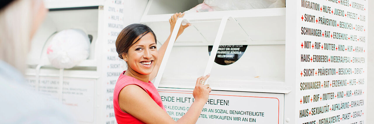 Junge Frau wirft einen Altkleidersack in einen Altkleidercontainer des Roten Kreuzes.