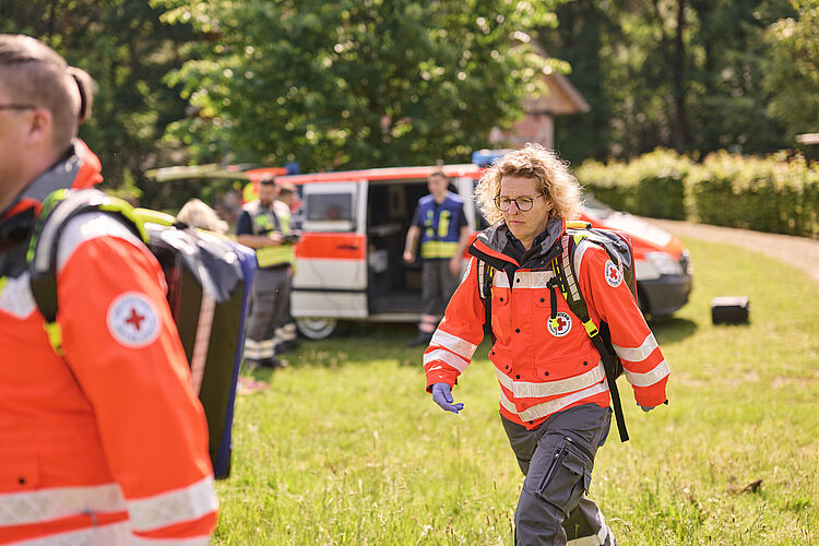 Bereitschaft Sanitätshelfer in EInsatzkleidung laufen über Wiese.