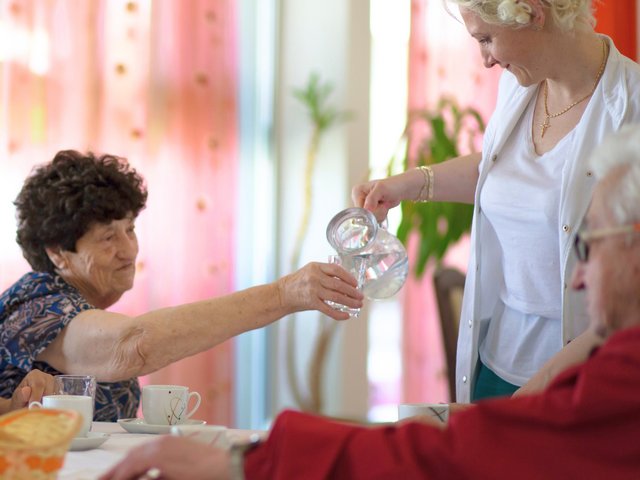 DRK-Mitarbeiterin schenkt Seniorinnen und Senioren frisches Wasser ein.