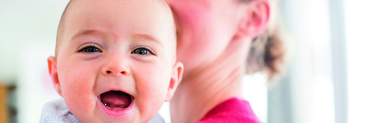 Mutter mit lächelndem Baby auf dem Arm.